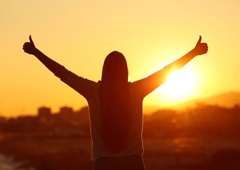 Backlight Of A Woman Raising Arms With Thumbs Up