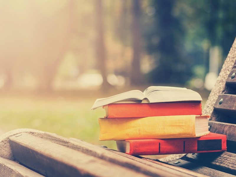 Stack of hardback books and Open book lying on bench