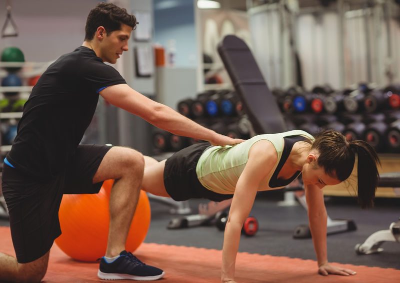 Fit Woman Working Out With Trainer At The Gym