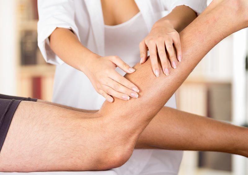 Closeup Female Physio Therapist Hands Working On Male Patients Legs, Blurry Clinic Background