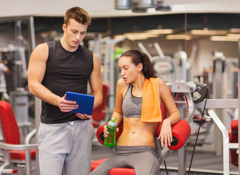Smiling Young Woman With Personal Trainer In Gym