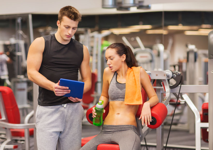Smiling Young Woman With Personal Trainer In Gym